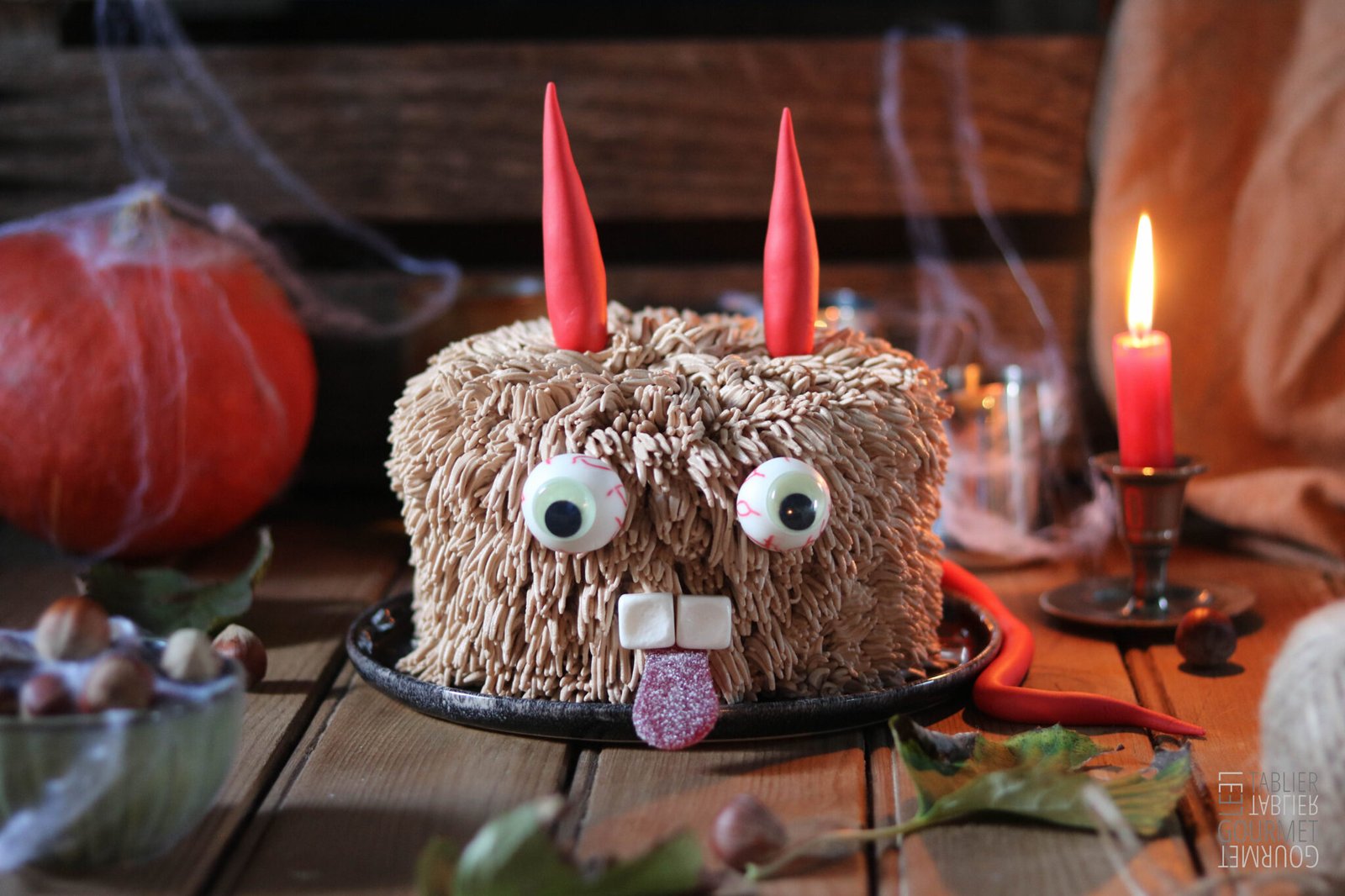 Le gâteau d'Halloween est un shag cake recouvert d'une ganache au chocolat, avec des cornes et une queue en pâte à sucre rouge. Il a des yeux, des dents et une bouche en bonbon. Le tout est présenté dans une ambiance maison hantée