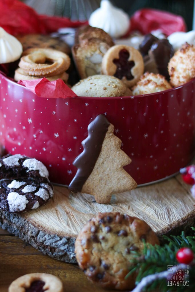 Gros plan sur un biscuit au blé noir posé devant une boite à biscuits débordante de gâteaux 