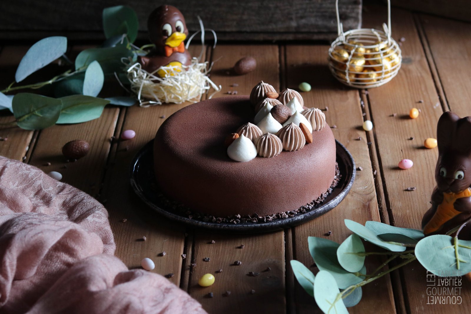 Un enetremets de Pâques avec de la chantilly et de la ganache pochées dessus et une mise en scène avec des sujets en chocolat