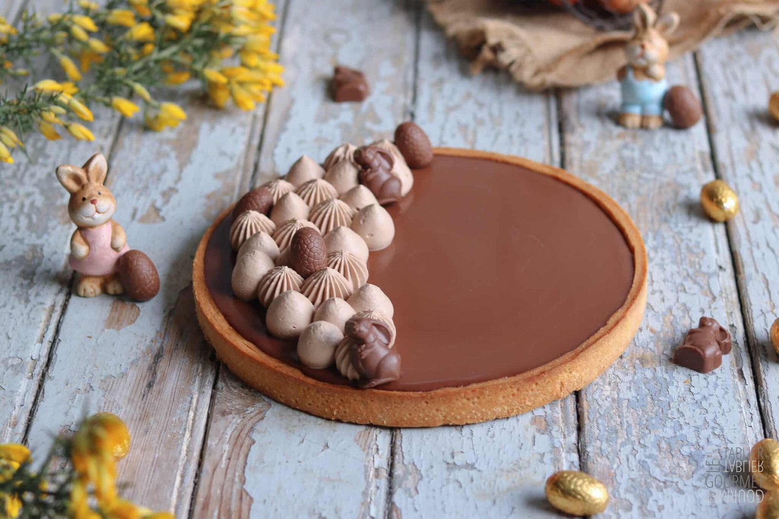 Une tarte au chocolat et caramel dans un décor de Pâques avec des petits oeufs et des lapins