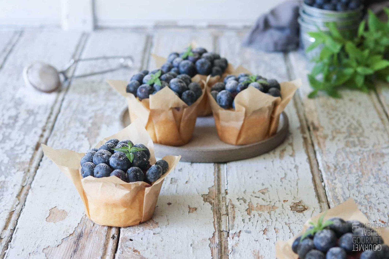 Une table avec plein de muffins recouverts de myrtille et de feuilles de menthe