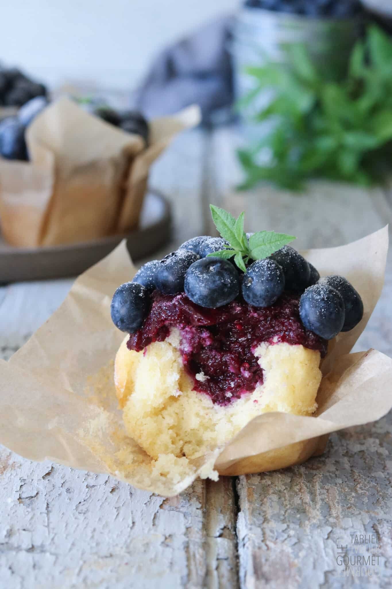 Gros plan sur un muffin entamé et débordant de confit de myrtilles et framboises